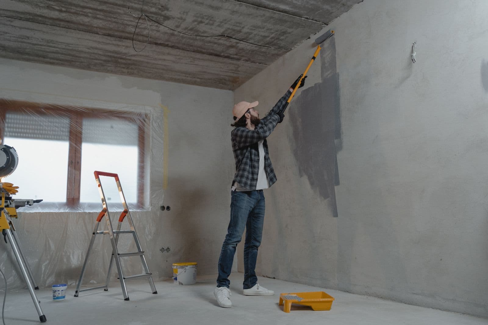 Painter rolling a wall with window protection and drop cloths in place